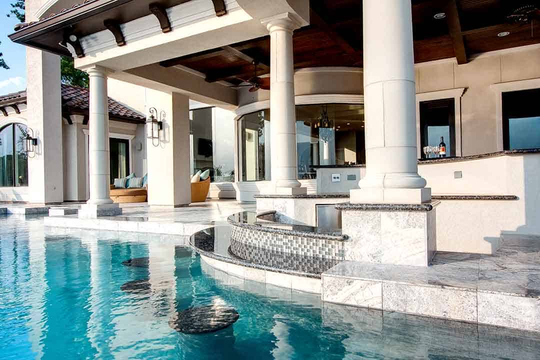 Elegant poolside patio with outdoor kitchen and white columns in The Woodlands